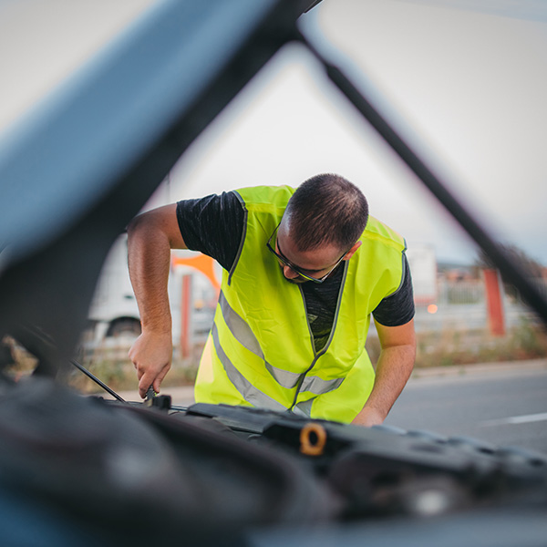 Mechanic wearing yellow vest and repairing broken car on road