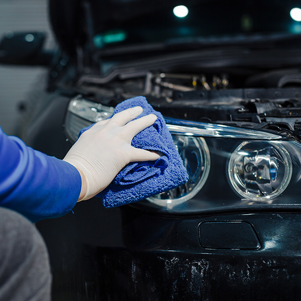 Mechanic cleaning car headlight with blue cloth