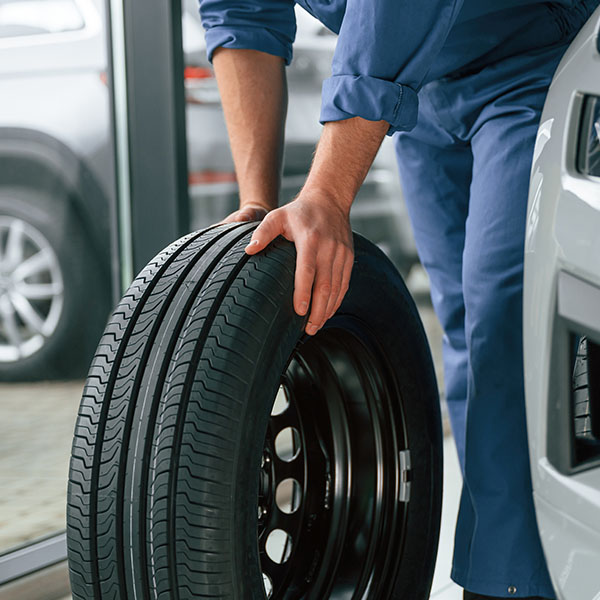 Mechanic holding car tire in front of car